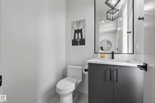 Powder room featuring a sleek vanity with a built-in sink, dark cabinetry, a framed mirror, and a modern toilet - 7314 Morgan Road Nw, Edmonton, AB - Indoor Photo Showing Bathroom