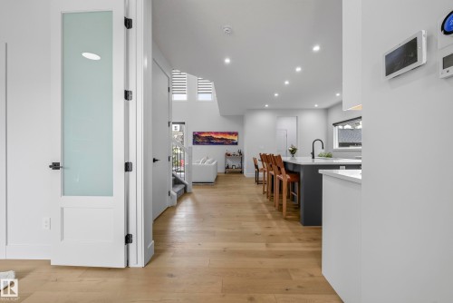 Light wood-finish flooring extending throughout, contemporary frosted glass paneled door, recessed lighting, and a kitchen island with seating - 7314 Morgan Road Nw, Edmonton, AB - Indoor