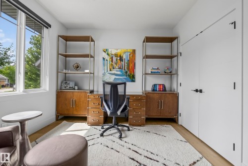 Wood-finish flooring, built-in shelving, expansive window, and contemporary white doors with dark hardware - 7314 Morgan Road Nw, Edmonton, AB - Indoor Photo Showing Other Room
