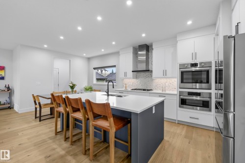 Modern kitchen featuring a large central island, light wood-finish flooring, white cabinetry, stainless steel appliances, and recessed lighting - 7314 Morgan Road Nw, Edmonton, AB - Indoor Photo Showing Kitchen With Upgraded Kitchen
