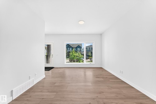 Recessed ceiling light, expansive window, wood-finish flooring, white trim, and a white entry door - 3816 Chrustawka Place Sw, Edmonton, AB - Indoor Photo Showing Other Room