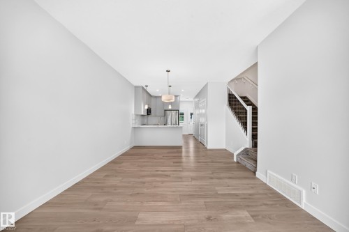 Open-concept living space featuring wood-finish flooring, a contemporary kitchen with light cabinetry, and a staircase with dark banisters - 3816 Chrustawka Place Sw, Edmonton, AB - Indoor Photo Showing Other Room