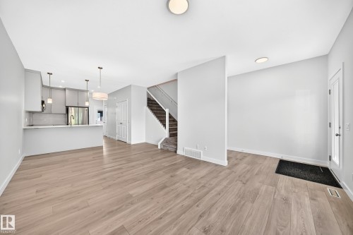 Open-concept living area with wood-finish flooring, a contemporary kitchen featuring light-toned cabinetry, stainless steel appliances, and a central island - 3816 Chrustawka Place Sw, Edmonton, AB - Indoor