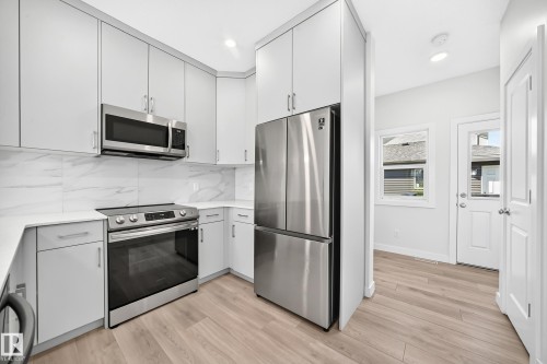Kitchen featuring light-toned cabinetry, stainless steel appliances, white countertops, and a white tile backsplash - 3816 Chrustawka Place Sw, Edmonton, AB - Indoor Photo Showing Kitchen With Upgraded Kitchen