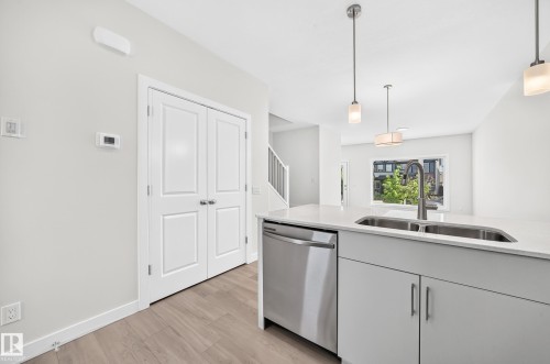 Kitchen island with an undermount double basin sink, stainless steel dishwasher, and light gray cabinetry - 3816 Chrustawka Place Sw, Edmonton, AB - Indoor Photo Showing Kitchen With Double Sink