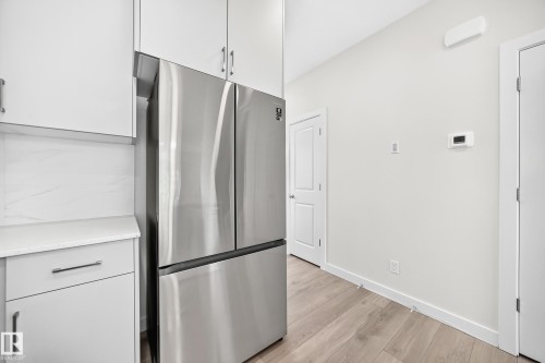 Stainless steel refrigerator, white cabinetry with silver-tone hardware, white countertops, wood-finish flooring, and light-toned walls - 3816 Chrustawka Place Sw, Edmonton, AB - Indoor