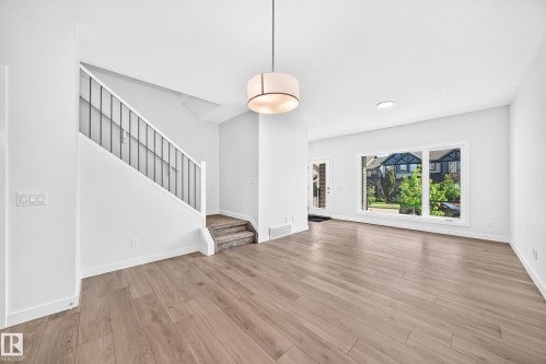 Wide plank wood-finish flooring throughout, prominent staircase with metal balusters, large front window, recessed ceiling lighting, and a drum pendant light fixture - 3816 Chrustawka Place Sw, Edmonton, AB - Indoor