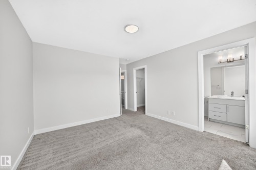 Plush gray carpeting throughout, neutral wall paint, overhead flush-mount lighting, and access to a bathroom featuring a vanity with under-sink storage and a wall-mounted light fixture - 3816 Chrustawka Place Sw, Edmonton, AB - Indoor Photo Showing Other Room
