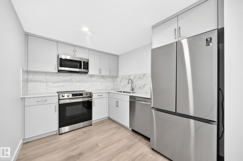 Contemporary kitchen featuring light gray cabinetry, stainless steel appliances, marble-look backsplash, light-toned wood-finish flooring, and recessed lighting - 3816 Chrustawka Place Sw, Edmonton, AB - Indoor Photo Showing Kitchen With Upgraded Kitchen