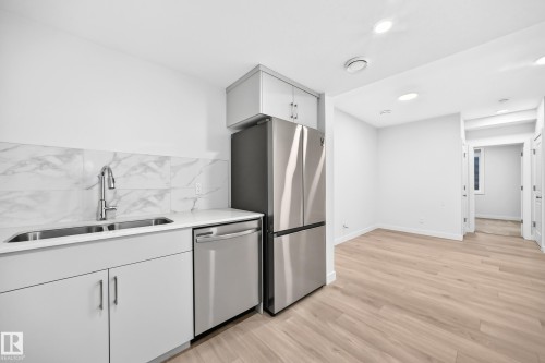 Kitchen featuring a double basin stainless steel sink with a high-arc faucet, white cabinetry, a white countertop, and a white tile backsplash - 3816 Chrustawka Place Sw, Edmonton, AB - Indoor Photo Showing Kitchen With Double Sink