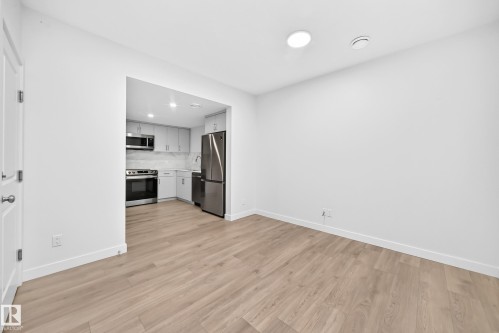 Light wood-finish flooring throughout, recessed lighting, and a kitchen featuring stainless steel appliances, light gray cabinetry, and a subway tile backsplash - 3816 Chrustawka Place Sw, Edmonton, AB - Indoor