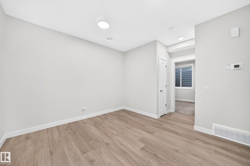 Light gray wall finishes, recessed lighting, wood-finish flooring, white interior door, and window - 3816 Chrustawka Place Sw, Edmonton, AB - Indoor Photo Showing Other Room