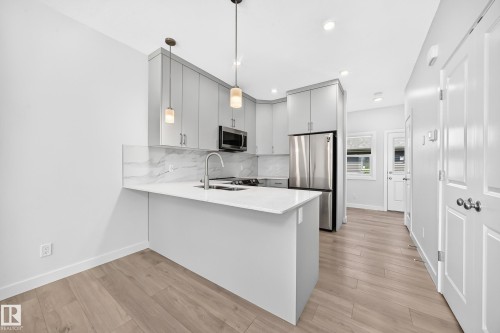 Modern kitchen featuring light gray cabinetry, stainless steel appliances, white countertops, and wood-finish flooring - 3816 Chrustawka Place Sw, Edmonton, AB - Indoor Photo Showing Kitchen With Upgraded Kitchen