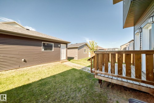 Expansive backyard featuring a wood deck with railing, manicured lawn, and a separate structure with a white entry door - 3816 Chrustawka Place Sw, Edmonton, AB - Outdoor With Exterior