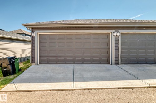 Two attached garage doors with panel detailing, exterior wall lanterns, and a concrete driveway - 3816 Chrustawka Place Sw, Edmonton, AB - Outdoor With Exterior