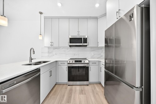 Kitchen featuring light cabinetry, stainless steel appliances, white countertops, a double basin sink, and wood-finish flooring - 3816 Chrustawka Place Sw, Edmonton, AB - Indoor Photo Showing Kitchen With Double Sink With Upgraded Kitchen