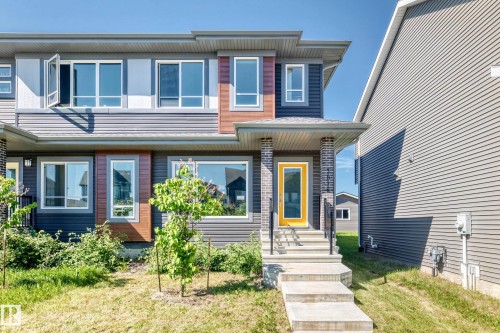 Contemporary exterior featuring dark horizontal siding, a covered entry with brick-clad columns, and a bright yellow front door - 3816 Chrustawka Place Sw, Edmonton, AB - Outdoor With Facade