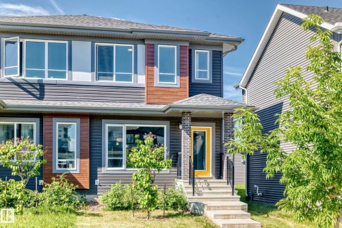 Modern exterior featuring dark horizontal siding, wood-finish accent panels, multiple large windows, a covered entry, and a vibrant yellow front door - 3816 Chrustawka Place Sw, Edmonton, AB - Outdoor With Facade