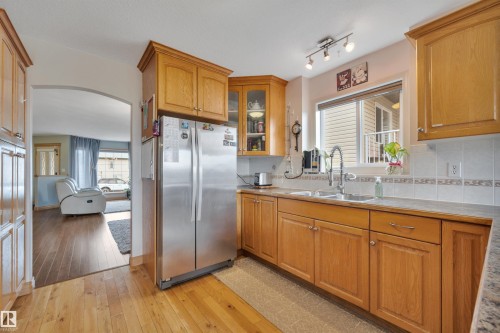 Kitchen featuring wood-finish cabinetry, stainless steel refrigerator, double basin sink, and tile backsplash - 4224 53 Ave, Wetaskiwin, AB - Indoor Photo Showing Kitchen With Double Sink