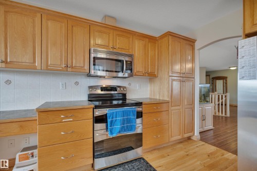 Wood-finish cabinetry, stainless steel microwave, stainless steel range, light-toned wood-finish flooring, and a tiled backsplash - 4224 53 Ave, Wetaskiwin, AB - Indoor Photo Showing Kitchen