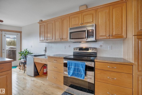 Kitchen featuring wood-finish cabinetry, stainless steel appliances, tiled backsplash, wood-finish flooring, and built-in desk area - 4224 53 Ave, Wetaskiwin, AB - Indoor Photo Showing Kitchen
