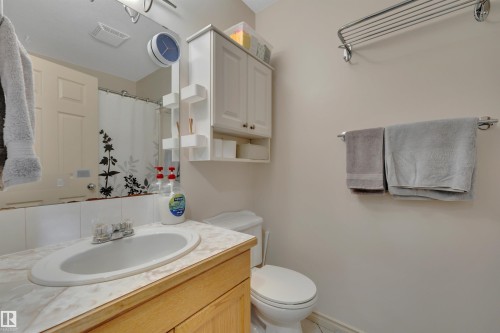 Vanity with an integrated sink and wood-finish cabinetry, mounted wall mirror, and toilet - 4224 53 Ave, Wetaskiwin, AB - Indoor Photo Showing Bathroom