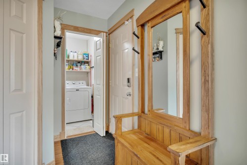 Entryway featuring wood-finish flooring, a built-in wooden hall tree with a mirror, and a pocket laundry area with a white washer - 4224 53 Ave, Wetaskiwin, AB - Indoor Photo Showing Other Room