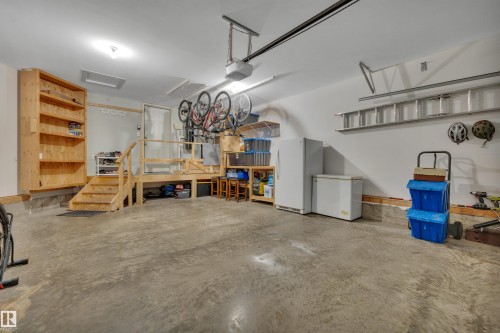 Garage space featuring a concrete floor, built-in wooden shelving, raised wooden platform with stairs, and overhead garage door opener - 4224 53 Ave, Wetaskiwin, AB - Indoor Photo Showing Garage