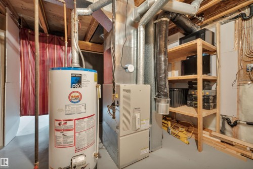 Utility area featuring a water heater, furnace, exposed ductwork, and built-in wood shelving - 4224 53 Ave, Wetaskiwin, AB - Indoor Photo Showing Basement