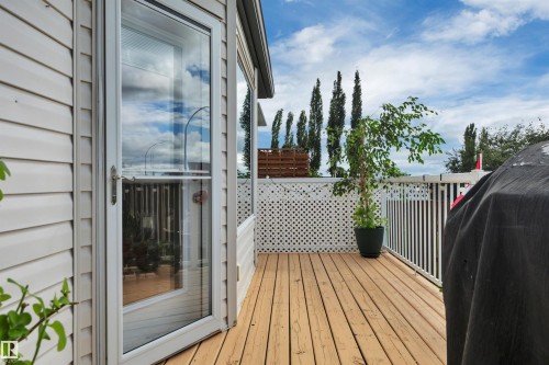 Spacious deck featuring wood-finish flooring, white lattice and vertical slat railings, and a full-light glass door - 4224 53 Ave, Wetaskiwin, AB - Outdoor With Deck Patio Veranda With Exterior