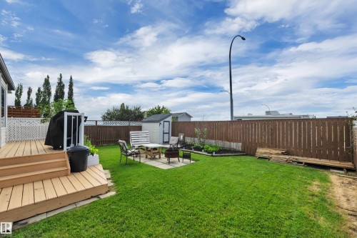 Expansive backyard featuring a wood deck, manicured lawn, paved patio area, wood fencing, and a storage shed - 4224 53 Ave, Wetaskiwin, AB - Outdoor With Deck Patio Veranda
