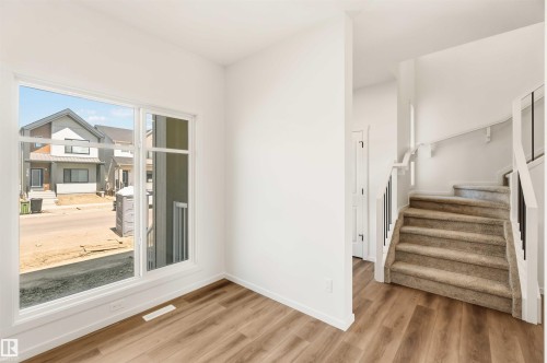 Bright interior space featuring wood-finish flooring, a large window with white trim, and a carpeted staircase with white and black railings - 265 Chappelle Drive Sw, Edmonton, AB - Indoor Photo Showing Other Room