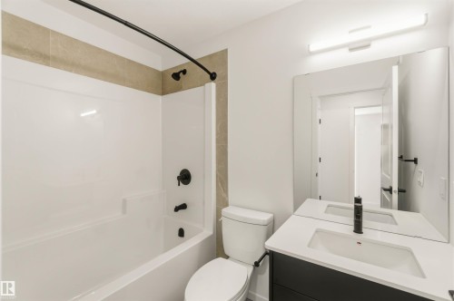 Full bathroom featuring a white tub and shower surround, matte black shower fixtures, a toilet, and a vanity with an integrated sink and matte black faucet - 265 Chappelle Drive Sw, Edmonton, AB - Indoor Photo Showing Bathroom