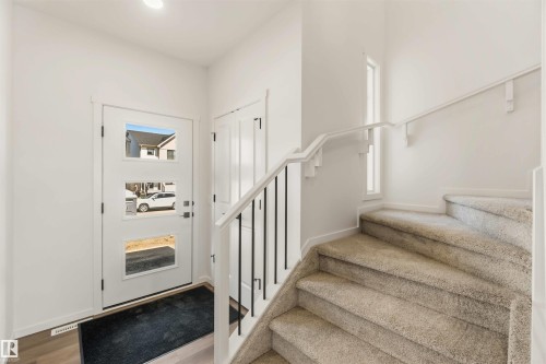 Entry foyer with wood-finish flooring, a contemporary front door featuring three clear glass panels, and a carpeted staircase with a white railing and black balusters - 265 Chappelle Drive Sw, Edmonton, AB - Indoor Photo Showing Other Room
