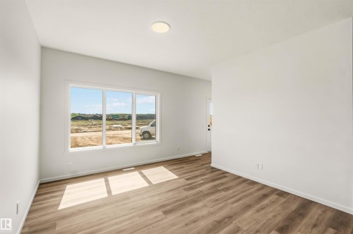 Spacious room featuring wood-finish flooring, white walls, and a prominent three-panel window - 265 Chappelle Drive Sw, Edmonton, AB - Indoor Photo Showing Other Room