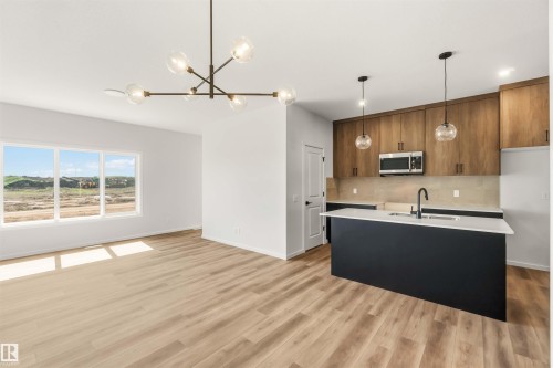 Open-concept living space featuring wood-finish flooring, a contemporary chandelier, and a kitchen island with seating - 265 Chappelle Drive Sw, Edmonton, AB - Indoor Photo Showing Kitchen