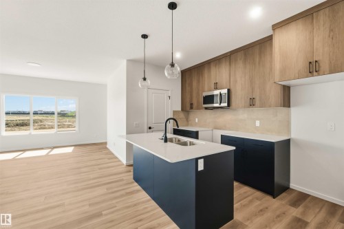 Modern kitchen showcasing a central island with an undermount sink, pendant lighting, wood-finish flooring, stainless steel microwave, and wood-finish cabinetry - 265 Chappelle Drive Sw, Edmonton, AB - Indoor Photo Showing Kitchen With Double Sink With Upgraded Kitchen
