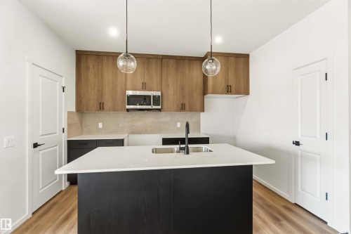 Kitchen featuring an island with an undermount sink, quartz countertop, and black base cabinetry - 265 Chappelle Drive Sw, Edmonton, AB - Indoor Photo Showing Kitchen With Double Sink