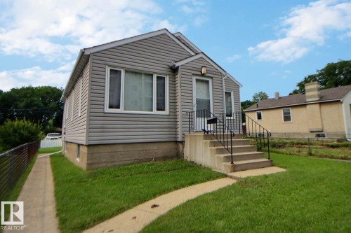 Siding exterior, concrete front steps, wrought iron handrails, front entry door with overhead light fixture, and a front yard with established grass - 11336 83 Street Nw, Edmonton, AB - Outdoor