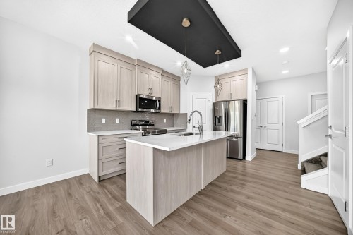 Kitchen featuring light wood-finish cabinetry, stainless steel appliances, a white island with an undermount sink, and a contrasting black ceiling accent with pendant lighting - 8823 Carson Way Sw, Edmonton, AB - Indoor Photo Showing Kitchen With Upgraded Kitchen
