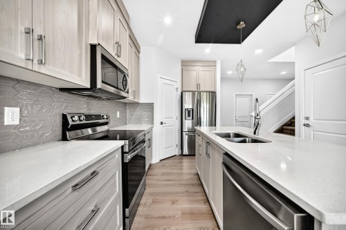 Well-appointed kitchen featuring light wood-finish cabinetry, stainless steel appliances, light-toned countertops, and wood-finish flooring - 8823 Carson Way Sw, Edmonton, AB - Indoor Photo Showing Kitchen With Double Sink With Upgraded Kitchen