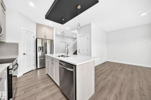 Modern kitchen featuring a central island with an undermount sink, stainless steel appliances, and light wood-finish cabinetry - 8823 Carson Way Sw, Edmonton, AB - Indoor Photo Showing Kitchen With Double Sink With Upgraded Kitchen