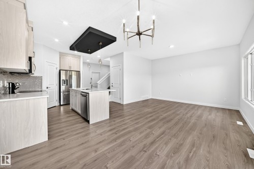 Open-concept living area featuring wood-finish flooring, a kitchen island with integrated sink, stainless steel appliances, and sleek overhead lighting - 8823 Carson Way Sw, Edmonton, AB - Indoor Photo Showing Kitchen With Upgraded Kitchen