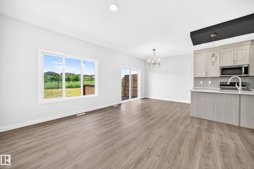 Wood-finish flooring, white walls, large window, sliding glass door, and kitchen with light-toned cabinetry - 8823 Carson Way Sw, Edmonton, AB - Indoor Photo Showing Kitchen