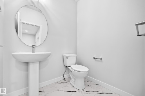 Pedestal sink with a circular mirror, modern toilet, and large format floor tiles - 8823 Carson Way Sw, Edmonton, AB - Indoor Photo Showing Bathroom