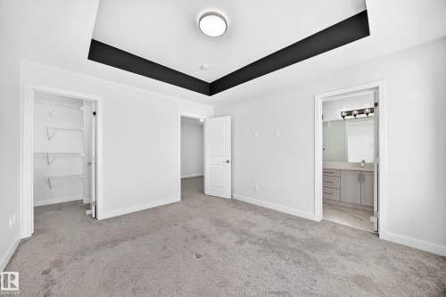Tray ceiling with accent trim, carpeted flooring, built-in closet shelving, and an en-suite bathroom with a vanity and mirror - 8823 Carson Way Sw, Edmonton, AB - Indoor Photo Showing Other Room