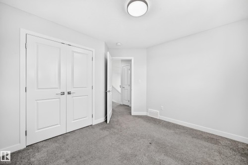 Neutral wall paint with gray carpeting, featuring a modern flush-mount ceiling light and white panel doors - 8823 Carson Way Sw, Edmonton, AB - Indoor Photo Showing Other Room