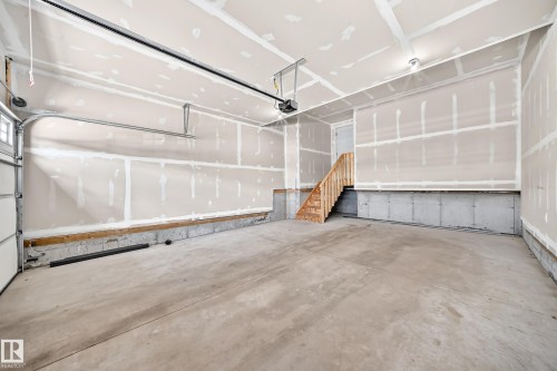 Spacious garage with unfinished drywall, concrete flooring, exposed concrete foundation, built-in wooden stairs, and an automatic garage door opener - 8823 Carson Way Sw, Edmonton, AB - Indoor Photo Showing Garage