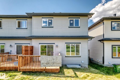 Rear exterior featuring light grey siding, multiple windows with dark trim, a wooden deck with railings, and two sliding glass doors - 8823 Carson Way Sw, Edmonton, AB - Outdoor With Exterior