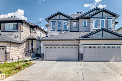Exterior featuring light-toned siding, dark trim accents, multiple windows, a prominent front entry, and a two-car garage - 8823 Carson Way Sw, Edmonton, AB - Outdoor With Facade